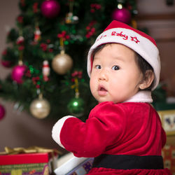 Cute baby girl wearing santa hat against christmas tree at home