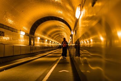 Rear view of woman walking in illuminated tunnel