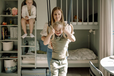 Mother helping son with down syndrome swinging on gymnastics rings in bedroom