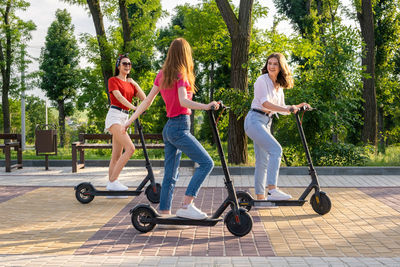 Three young girl friends on the electro scooters having fun in city street at summer day