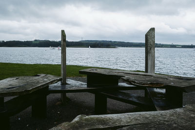 Wooden bench by lake against sky