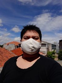 Portrait of young man wearing mask standing against sky