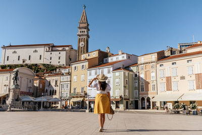 Rear view of young woman wearing standing in square of idyllic town of piran, slovenia