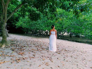 Rear view of woman standing on sand against trees