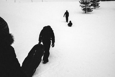 Rear view of people walking with sleds on snow covered field