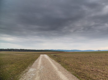 Empty road amidst field against sky