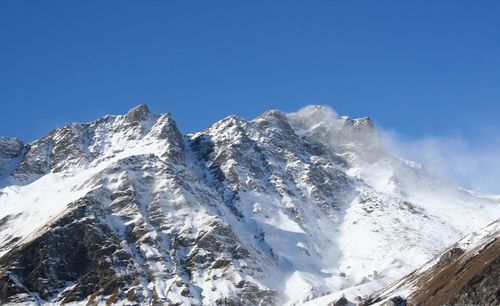 Low angle view of snowcapped mountains against clear blue sky