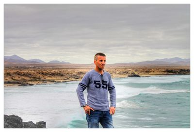 Man looking away while standing at beach against cloudy sky