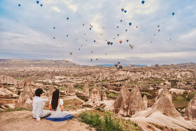 Rear view of people sitting on rock against sky