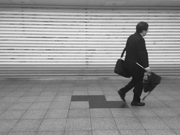 Full length of man holding umbrella while walking on paved street