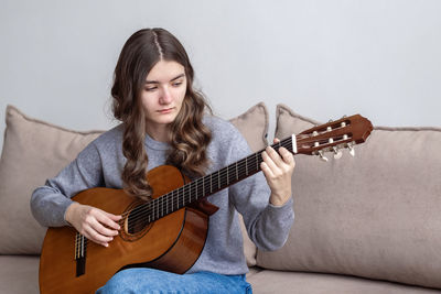 Girl playing guitar on sofa at home