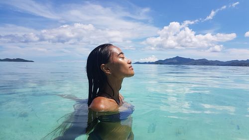 Side view of woman swimming in sea with eyes closed during summer