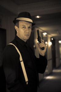 Portrait of man holding handgun while standing in corridor