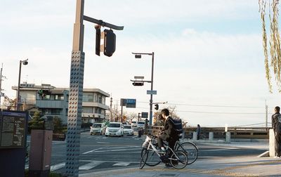 Man riding bicycle on street in city against sky