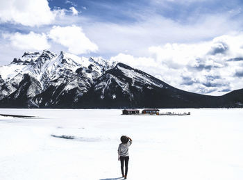 Rear view of woman looking at view while standing by frozen lake minnewanka against cloudy sky