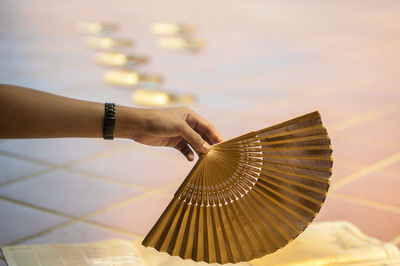 Cropped hand holding folding fan against tiled floor