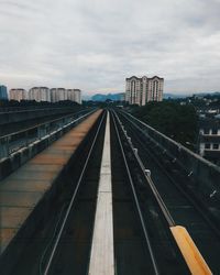 Railroad tracks in city against cloudy sky