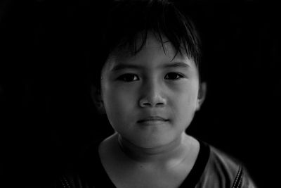 Close-up portrait of boy standing against black background