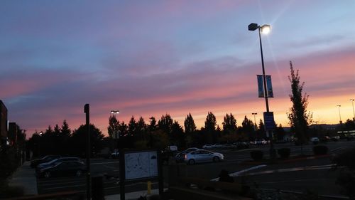 Cars parked on road against sky at sunset