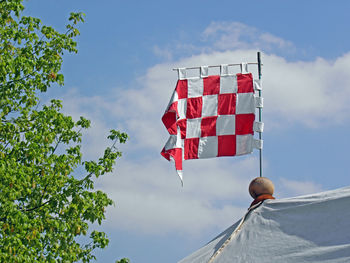 Low angle view of flag next to tree against cloudy sky