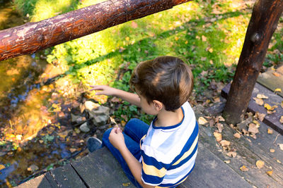 High angle view of a boy relaxing on wooden bridge above the creek in nature.