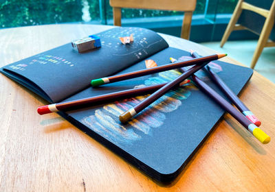 High angle view of colored pencils and art book on wooden table