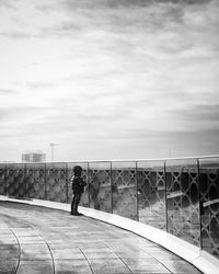 Man standing on railing against cloudy sky