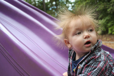 Close-up of toddler with spiked blond hair by purple slide at playground