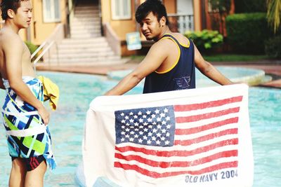 Rear view of man holding american flag while standing by swimming pool