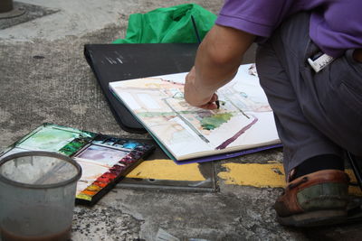 Low section of man painting in book on footpath