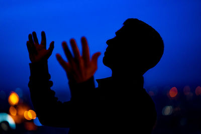 Side view of silhouette man gesturing against blue sky at night