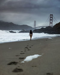 Rear view of woman walking at beach against sky