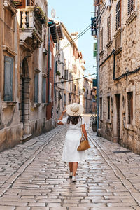 Rear view of young woman in white summer dress walking in street of picturesque old town