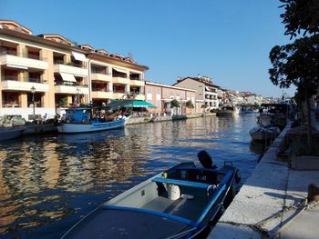 Boats moored in canal by buildings against clear sky