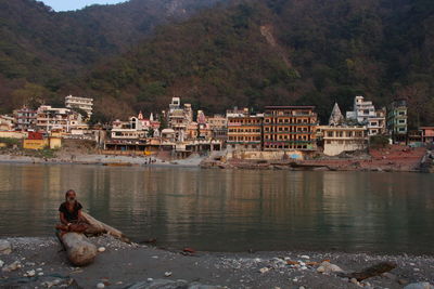 Sadhu sitting on driftwood by ganges river against city