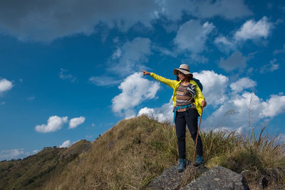 Mid adult woman gesturing on mountain against cloudy sky