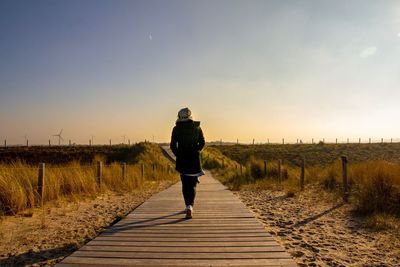 Rear view full length of woman walking amidst landscape on boardwalk