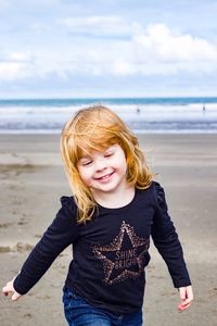 Portrait of smiling girl standing on beach against sky