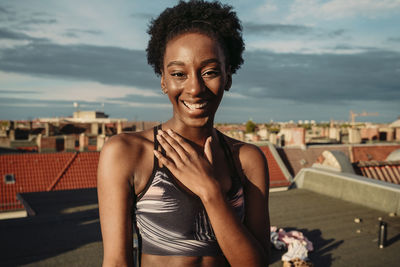 Portrait of happy female in sports clothing standing on rooftop during sunrise