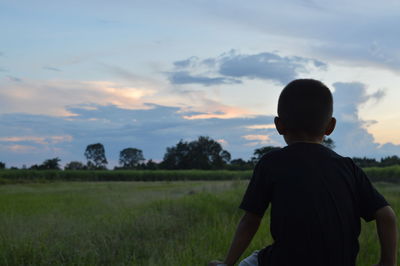 Rear view of man standing on field against sky during sunset