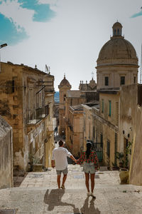 Rear view of people walking outside historic building against sky