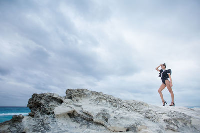 Man standing on rock at beach against sky