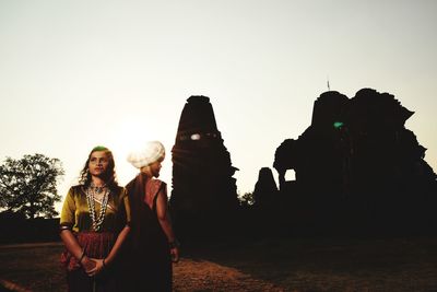 Women standing on land against clear sky during sunset