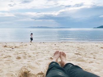 Low section of people relaxing on beach against sky