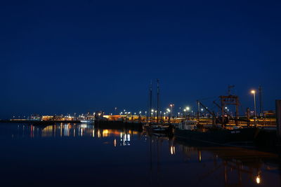 Boats moored at harbor against clear blue sky at night