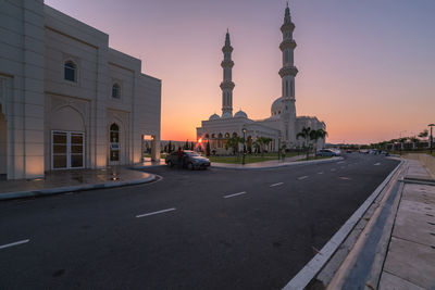 Cars on road by building against sky during sunset