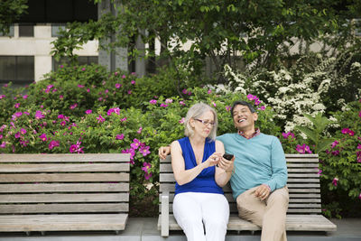 Happy mature couple using smart phone sitting on bench in park