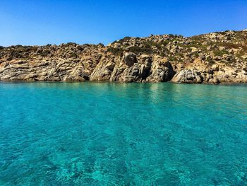 Rocky mountain by sea against clear blue sky