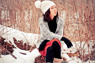 Young woman sitting on snow covered tree during winter