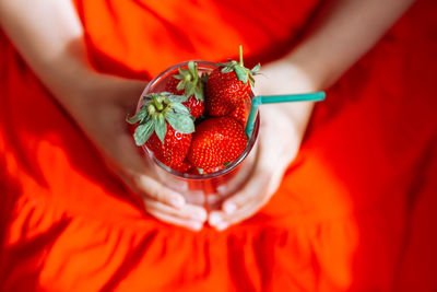 The hands of a little girl in a red skirt hold a glass with juicy strawberries.